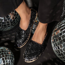 Load image into Gallery viewer, A foot of lady wearing a Sitara Espadrilles Black shoes for women kept upon a glittery ball.