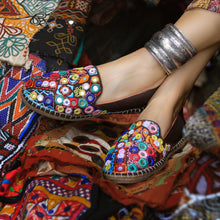 Load image into Gallery viewer, A foot of lady who have worn a Nomad Espadrilles Brown shoes for women kept upon a colorful cloth.