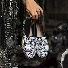 Load image into Gallery viewer, A woman holding a pair of Nomad Espadrilles Black shoes for women with a metal jewelry in the background.