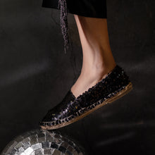 Load image into Gallery viewer, A foot of lady wearing a Sitara Espadrilles Black, ladies shoe kept on a glittery ball.
