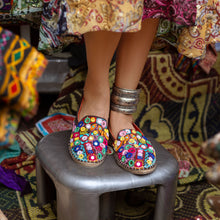 Load image into Gallery viewer, A foot of lady who have worn a Nomad Espadrilles Brown shoes for women kept upon a small stool with colorful fabric in the background.