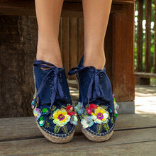 Load image into Gallery viewer, a girl standing on a wooden deck wearing a pair of blue espadrilles decorated with colorful flowers