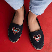 Load image into Gallery viewer, Feet of a model wearing black coloured Sweetheart Espadrilles ladies shoes with an evil eye protector design standing on a red surface