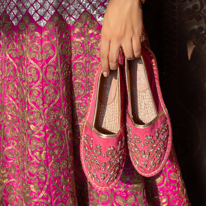 A woman holding a pair of Diva Rani Pink Espadrilles shoes for women with a beautiful cloth in the background.