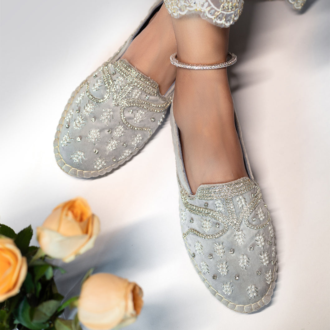 A foot of lady who have worn a Kaira Silver Espadrilles ladies shoes kept upon white background with some roses kept aside. 