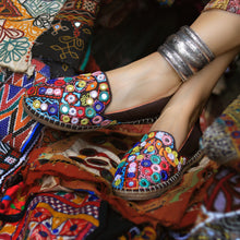 Load image into Gallery viewer, A foot of lady who have worn a Nomad Espadrilles Brown shoes for women kept upon a colorful cloth.
