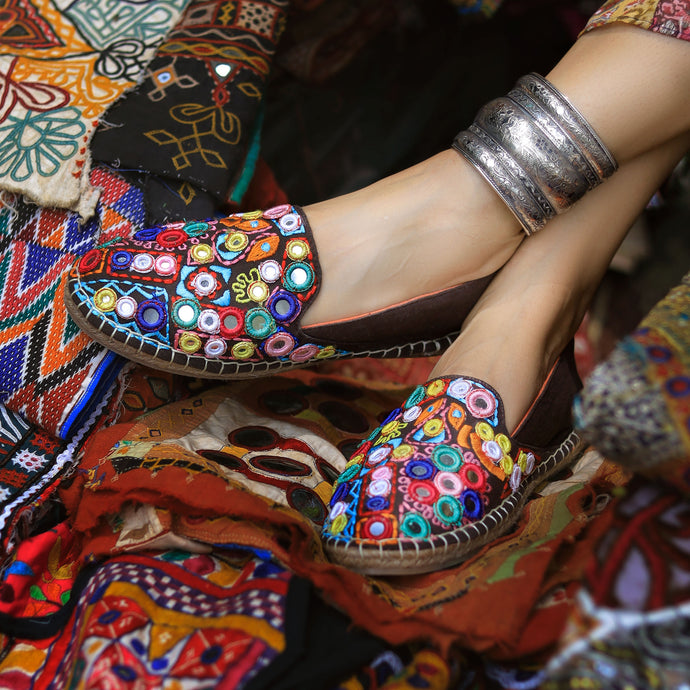A foot of lady who have worn a Nomad Espadrilles Brown shoes for women kept upon a colorful cloth.