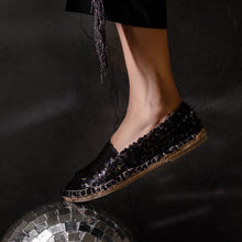Load image into Gallery viewer, A foot of lady wearing a Sitara Espadrilles Black, ladies shoe kept on a glittery ball.
