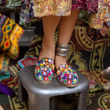 Load image into Gallery viewer, A foot of lady who have worn a Nomad Espadrilles Brown shoes for women kept upon a small stool with colorful fabric in the background.
