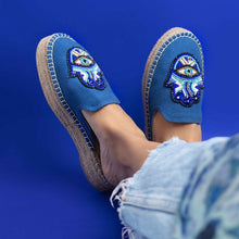 Load image into Gallery viewer, woman with crossed-leg wearing a pair of Hamsa blue espadrilles Platform having evil eye protector design, against a blue background.
