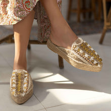 Load image into Gallery viewer, a woman&#39;s feet in golden Espadrilles on a white floor with a small detailing on them with a pattern around the bottom and sides
