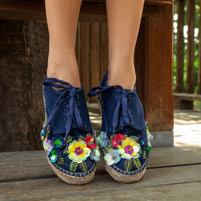 a girl standing on a wooden deck wearing a pair of blue espadrilles decorated with colorful flowers 