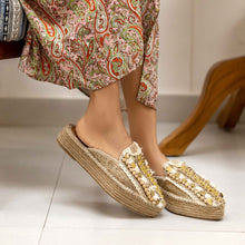 Load image into Gallery viewer, side view of a woman&#39;s feet in golden Espadrilles on a white floor with a small detailing on them with a pattern around the bottom and sides
