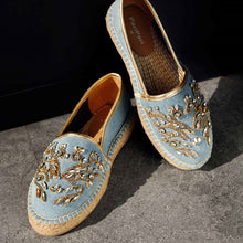 Load image into Gallery viewer, A pair of blue Espadrilles on a concrete floor with a small embroidery of gold detailing on them with a pattern around the bottom and sides
