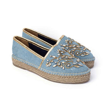 Load image into Gallery viewer, A pair of blue Espadrilles with a small embroidery of gold detailing on them with a pattern around the bottom and sides on a white background.
